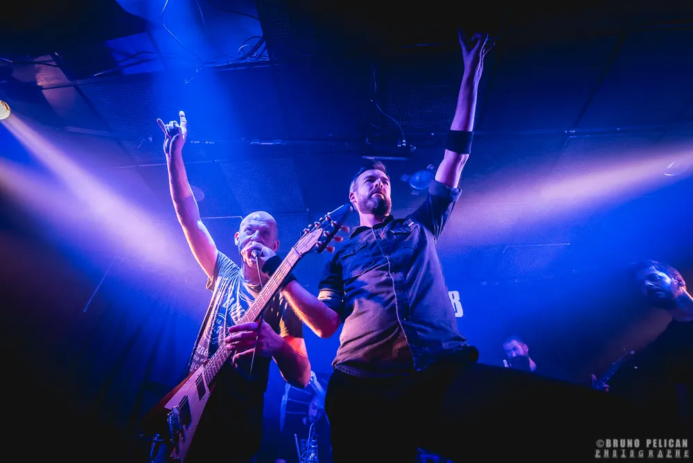 Le chanteur et un guitariste de Jackhammer, bras levés dans les projecteurs